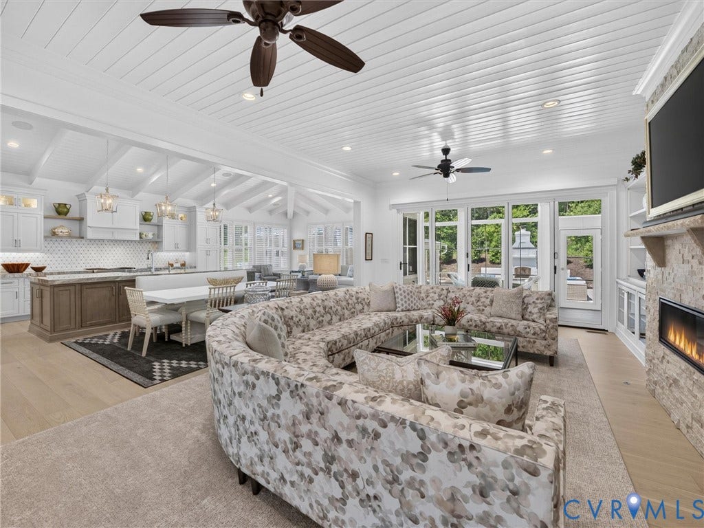 Expansive living area featuring a stone-clad fireplace with an electric insert, wood-finish flooring, and white paneled ceilings