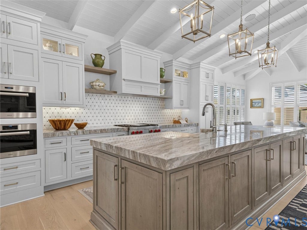 Gourmet kitchen featuring a large central island with integrated storage, white shaker cabinetry, stainless steel double wall ovens, a patterned tile backsplash, and a vaulted plank ceiling