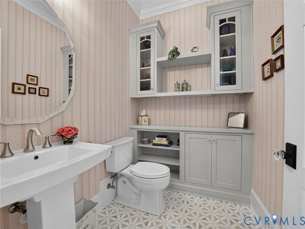 Powder room featuring a pedestal sink with brushed nickel fixtures, custom built-in cabinetry with glass-front uppers, a wall-mounted mirror, and patterned floor tiling