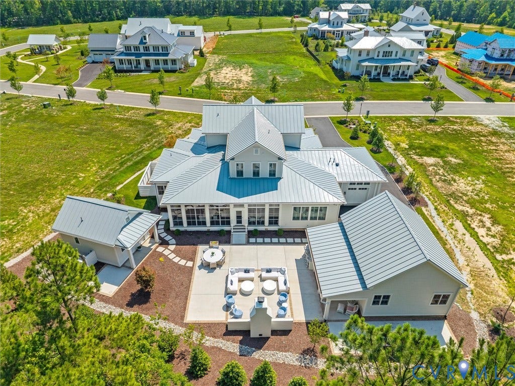 Contemporary residence featuring a light gray exterior, multiple gable roofs with metal roofing, a spacious rear patio, an attached three-car garage, and a detached auxiliary structure