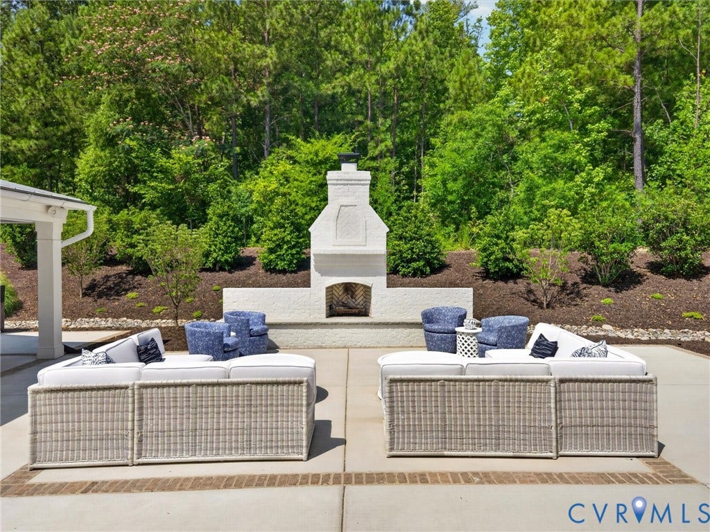 Outdoor patio area featuring a built-in white brick fireplace, concrete paver patio, and surrounding landscape beds with mature plantings