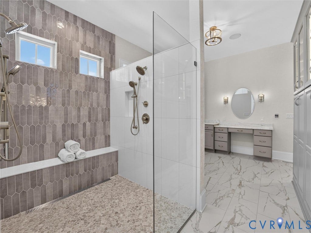 Spacious bathroom featuring a glass-enclosed shower with pebble-finish flooring and a built-in bench
