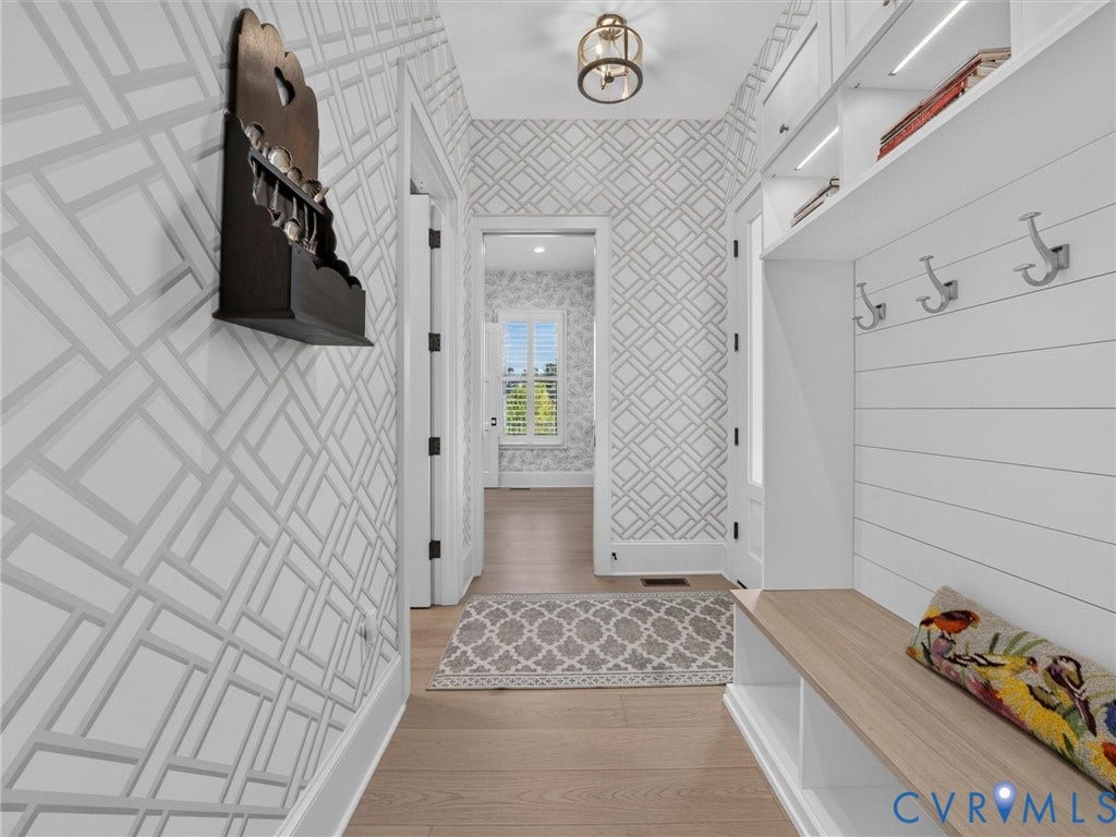 Hallway with light wood-finish flooring, geometric pattern wallpaper, and a built-in bench with integrated shelving
