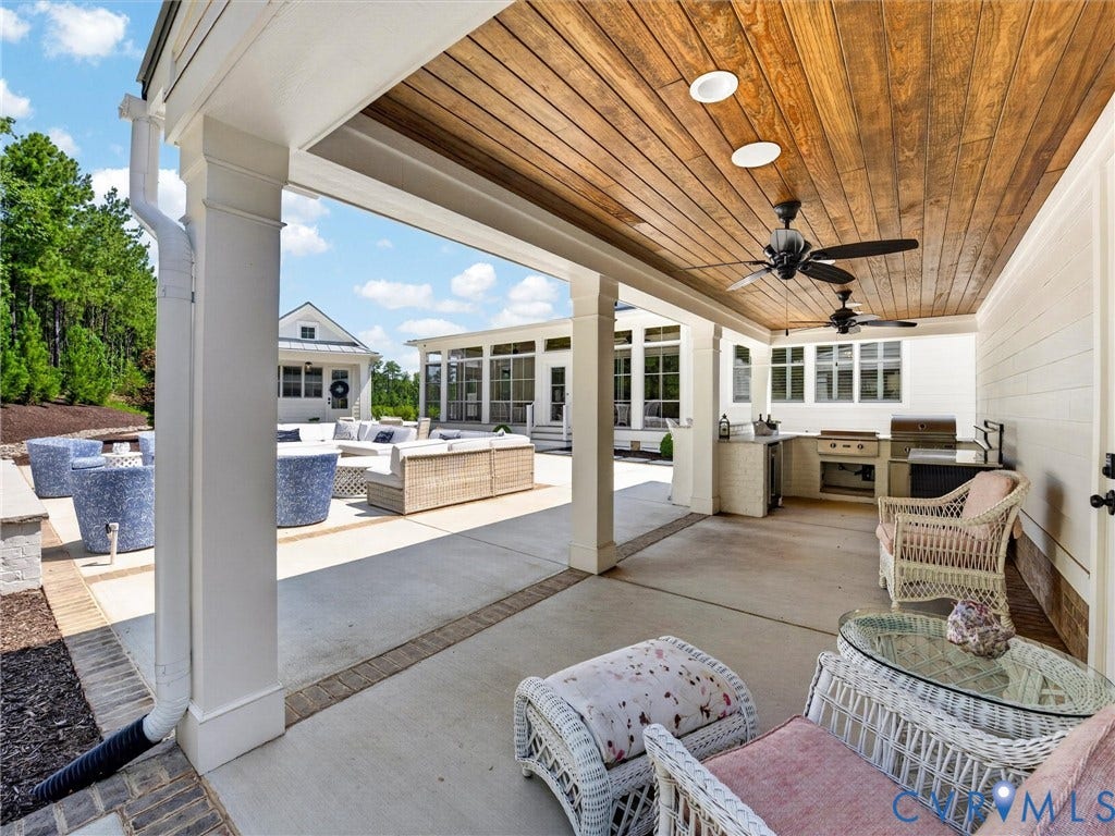 Expansive covered patio featuring a wood-panel ceiling with recessed lighting and ceiling fans, an integrated outdoor kitchen with built-in grill, concrete flooring, and white support columns