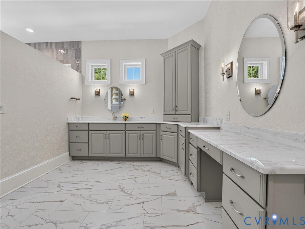 Spacious bathroom featuring large format tile flooring, extensive gray cabinetry with integrated storage, and contrasting white countertops