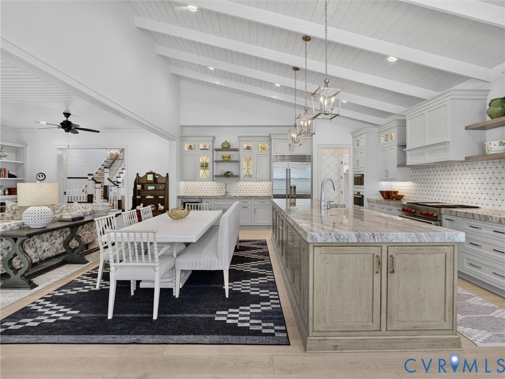 Open-concept kitchen and dining area featuring a vaulted ceiling with exposed beams, wood-finish flooring, a large kitchen island with a stone countertop, white cabinetry, and a patterned tile backsplash