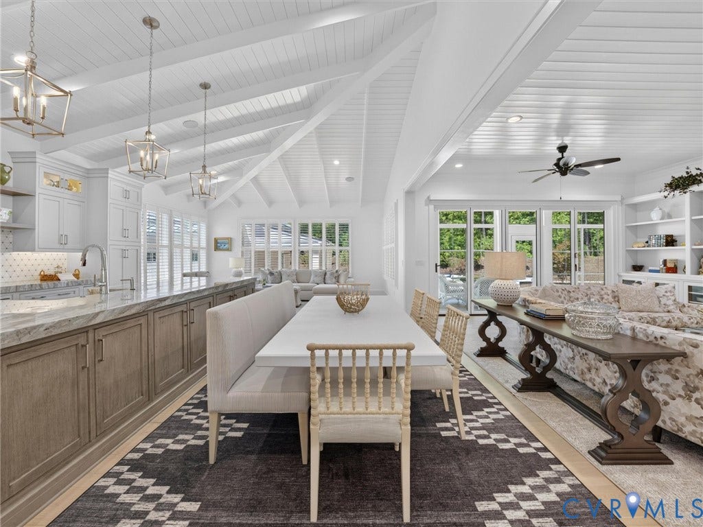 Open-concept interior featuring vaulted tongue-and-groove ceilings, a kitchen island with stone countertops and integrated sink, white shaker cabinetry, recessed lighting, and expansive glass doors opening to the exterior