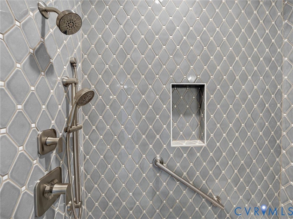 Shower enclosure featuring diamond-patterned tile, brushed nickel fixtures, a handheld showerhead, an integrated shower niche, and a grab bar