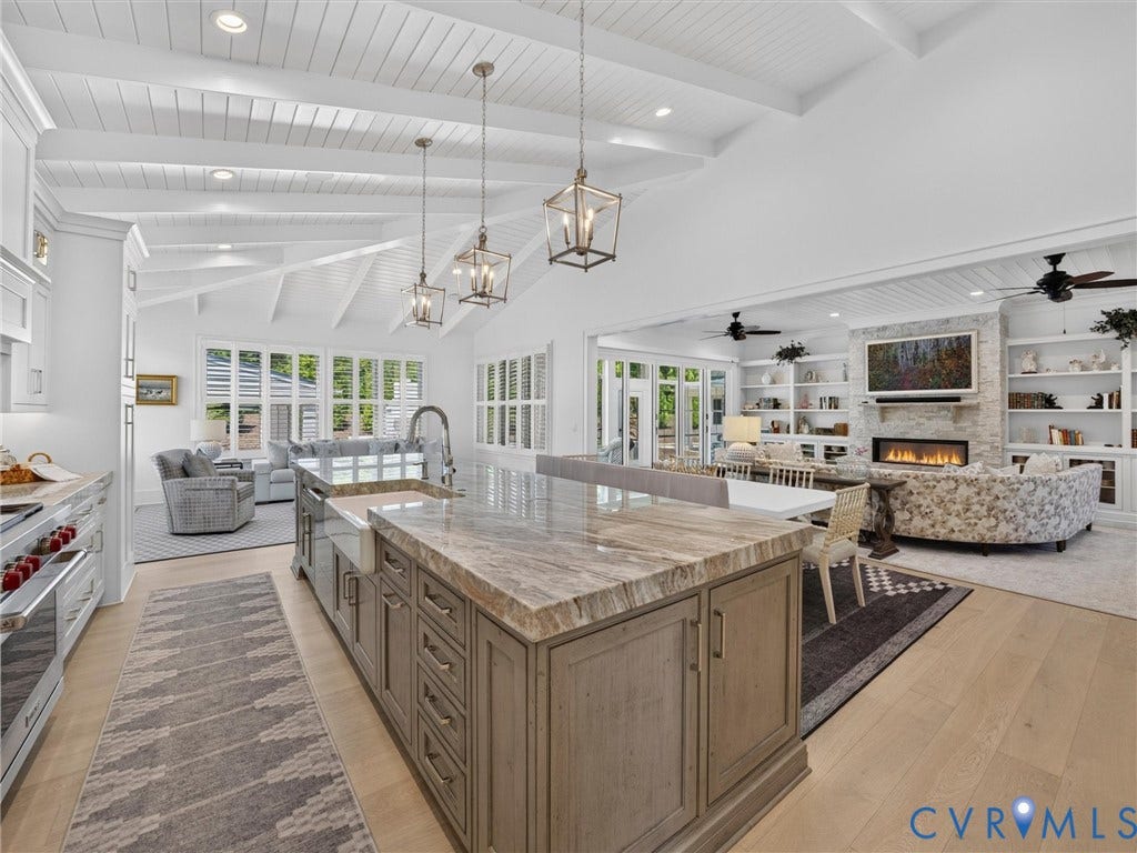 Spacious kitchen and living area featuring a large center island with a farmhouse sink, stone countertop, and pendant lighting