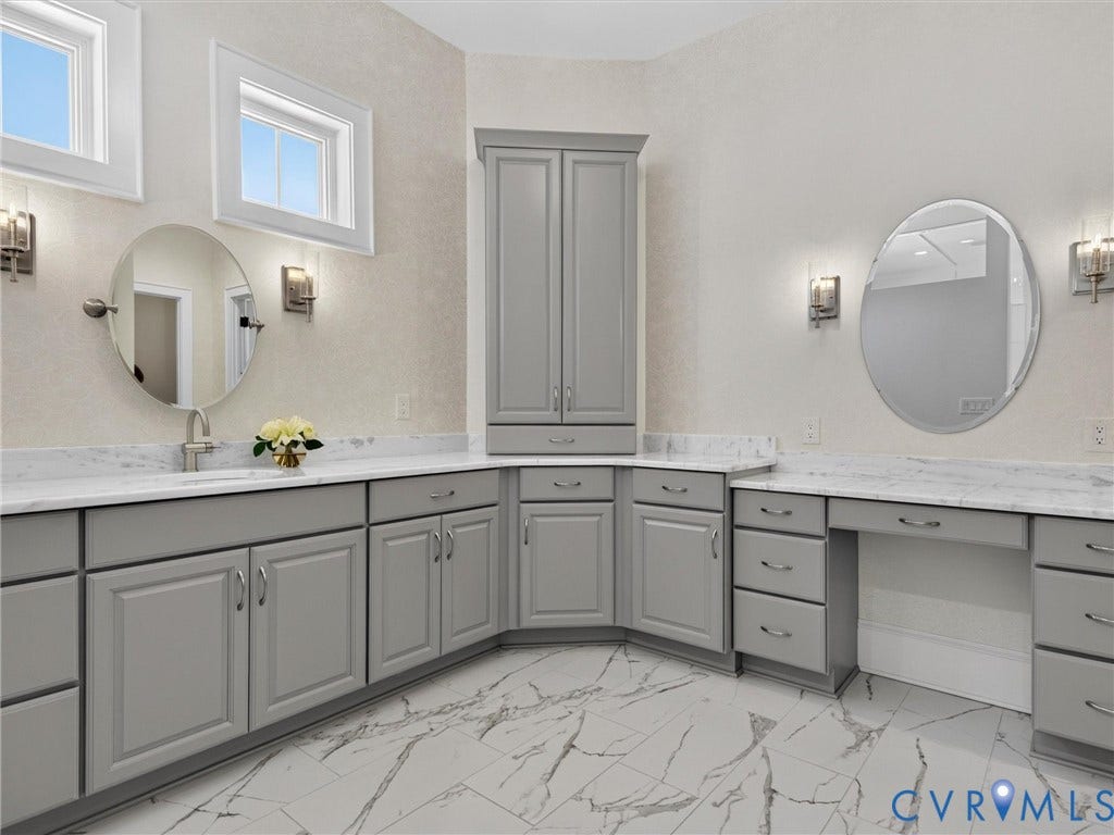 Spacious bathroom featuring marble-look tile flooring, light gray cabinetry with ample storage, white countertops, two framed mirrors, and a dedicated vanity area