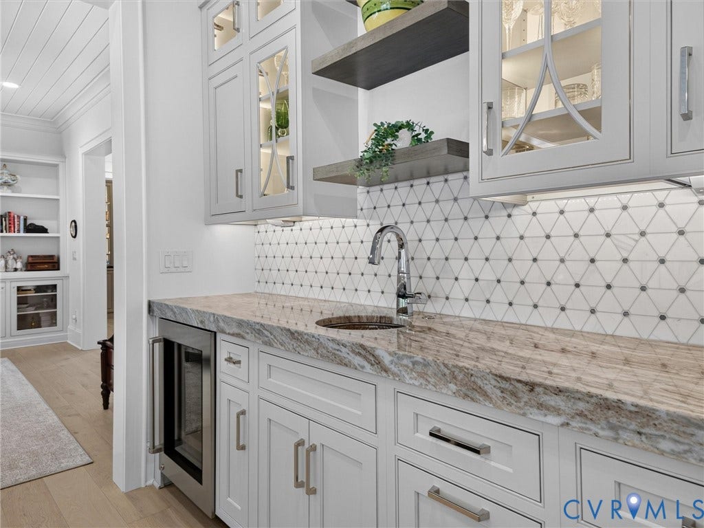 Custom wet bar featuring a polished chrome faucet, stone countertop, white shaker cabinetry, and a geometric tile backsplash