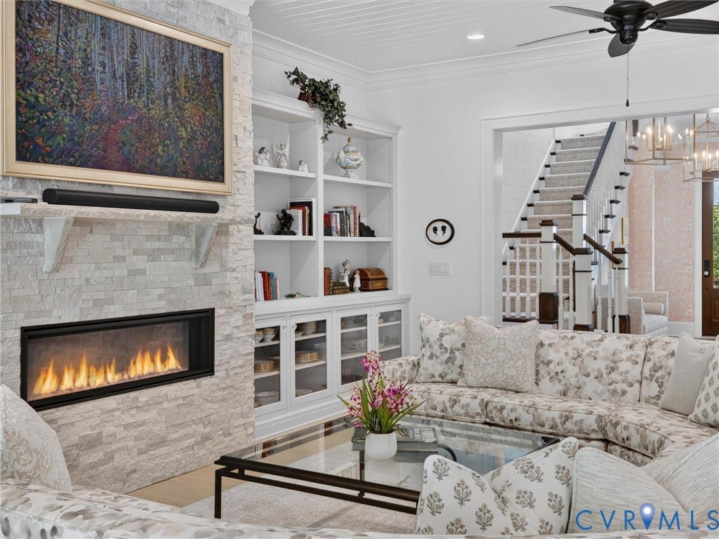 Living area featuring a floor-to-ceiling stacked stone fireplace, built-in shelving, glass-front cabinetry, and a ceiling fan