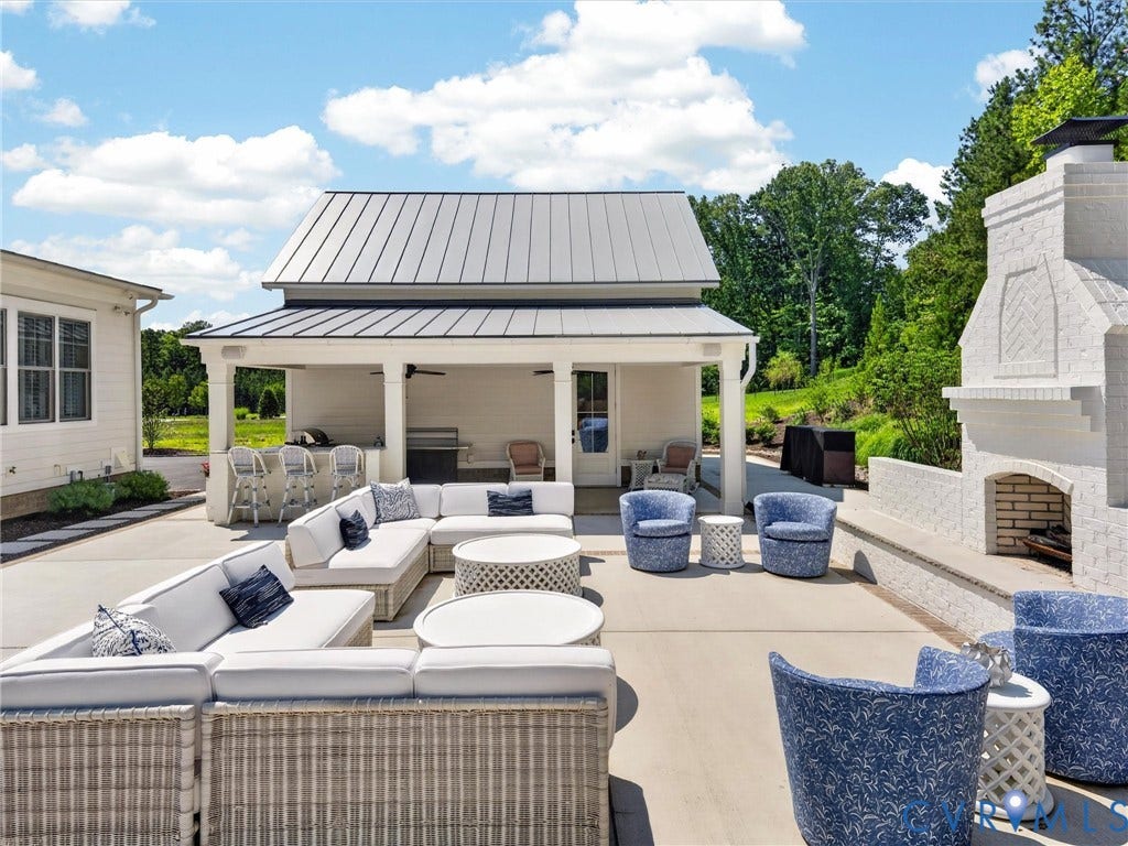 Expansive outdoor patio featuring a covered lounge area with built-in bar, white brick fireplace, and a light-colored concrete surface