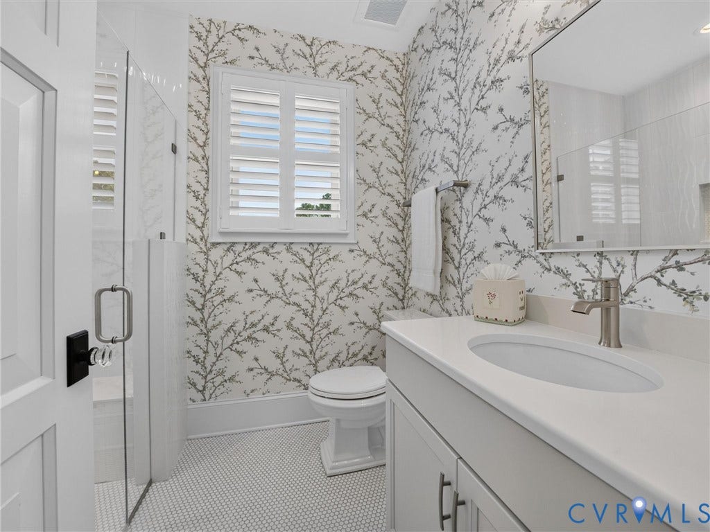 Bathroom featuring patterned wallpaper, a white vanity with an integrated sink, brushed nickel fixtures, a glass-enclosed shower, and hexagonal tile flooring