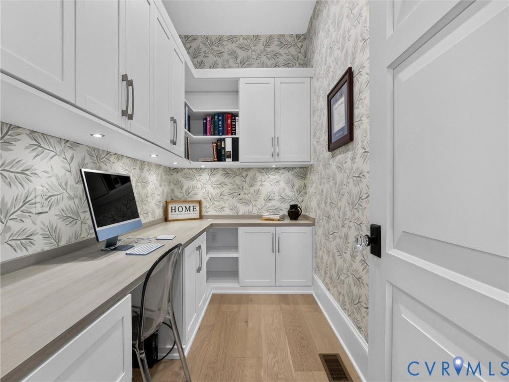 Built-in desk with L-shaped wood-finish countertop, under-cabinet lighting, and white shaker-style cabinetry