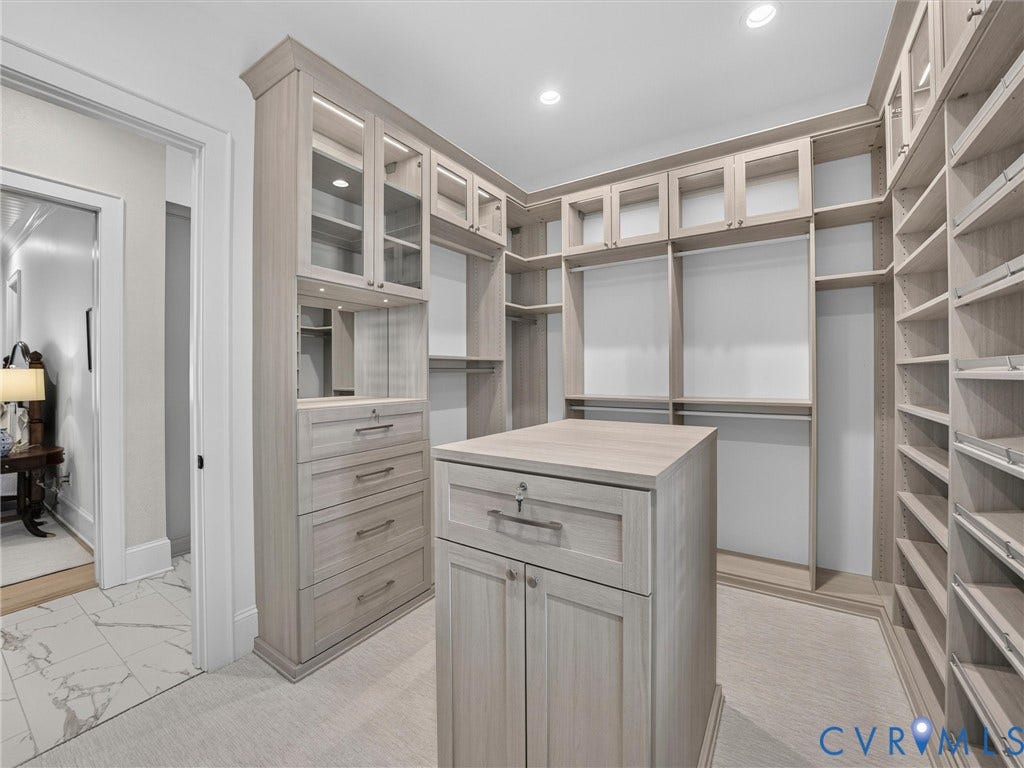 Custom closet system featuring light wood-finish cabinetry, glass-front upper cabinets, built-in shelving, and a central island with drawers