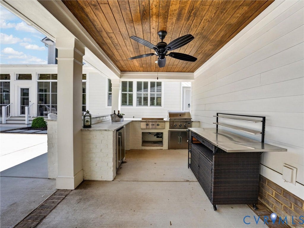 Covered outdoor kitchen featuring a wood-finish ceiling, built-in grill, integrated beverage refrigerator, stone countertop, and shiplap-style wall