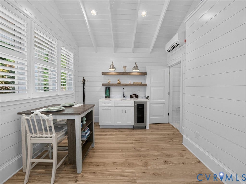 Open-concept space featuring wood-finish flooring, white shiplap walls, and a vaulted ceiling with exposed beams