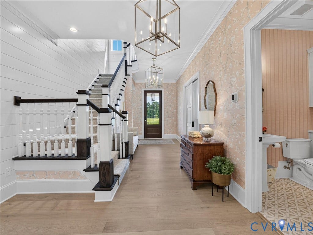 Entryway featuring light wood-finish flooring, a grand staircase with white balusters and dark newel posts, and decorative wallpaper accents