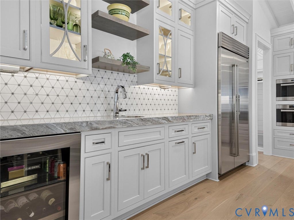 Custom wet bar featuring light gray cabinetry, under-cabinet lighting, a geometric tile backsplash, and a built-in beverage refrigerator