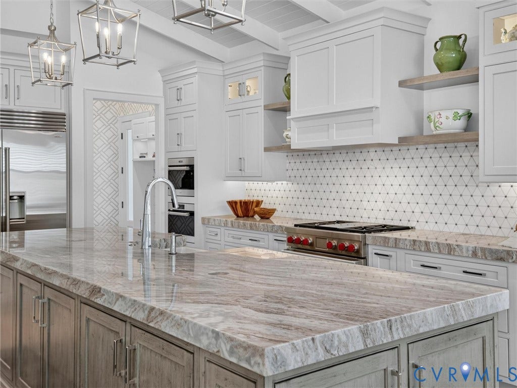 Spacious kitchen featuring a large island with a natural stone countertop, white shaker cabinetry, stainless steel appliances, and a geometric tile backsplash