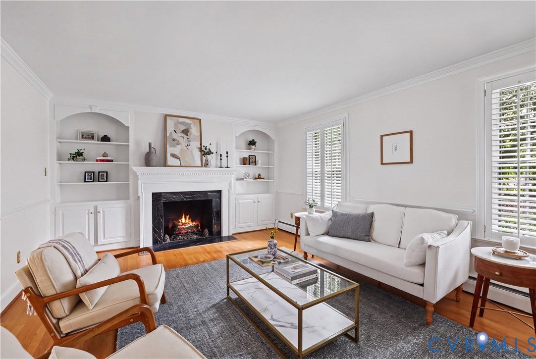5418 Cary Street Road, Richmond, VA 23226 Fireplace featuring a dark stone surround and decorative mantle, flanked by built-in arched cabinetry with shelving, wood-finish flooring, and window shutters