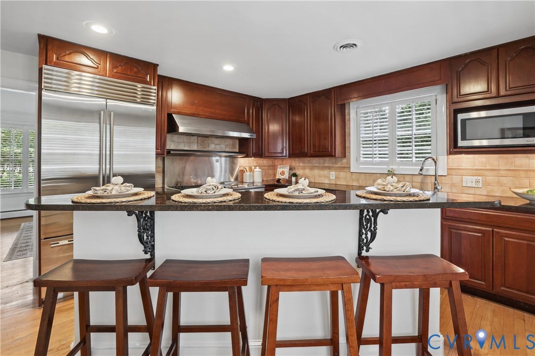 5418 Cary Street Road, Richmond, VA 23226 Kitchen featuring stained wood cabinetry, stone countertops with an integrated breakfast bar, stainless steel refrigerator, built-in microwave, and subway tile backsplash