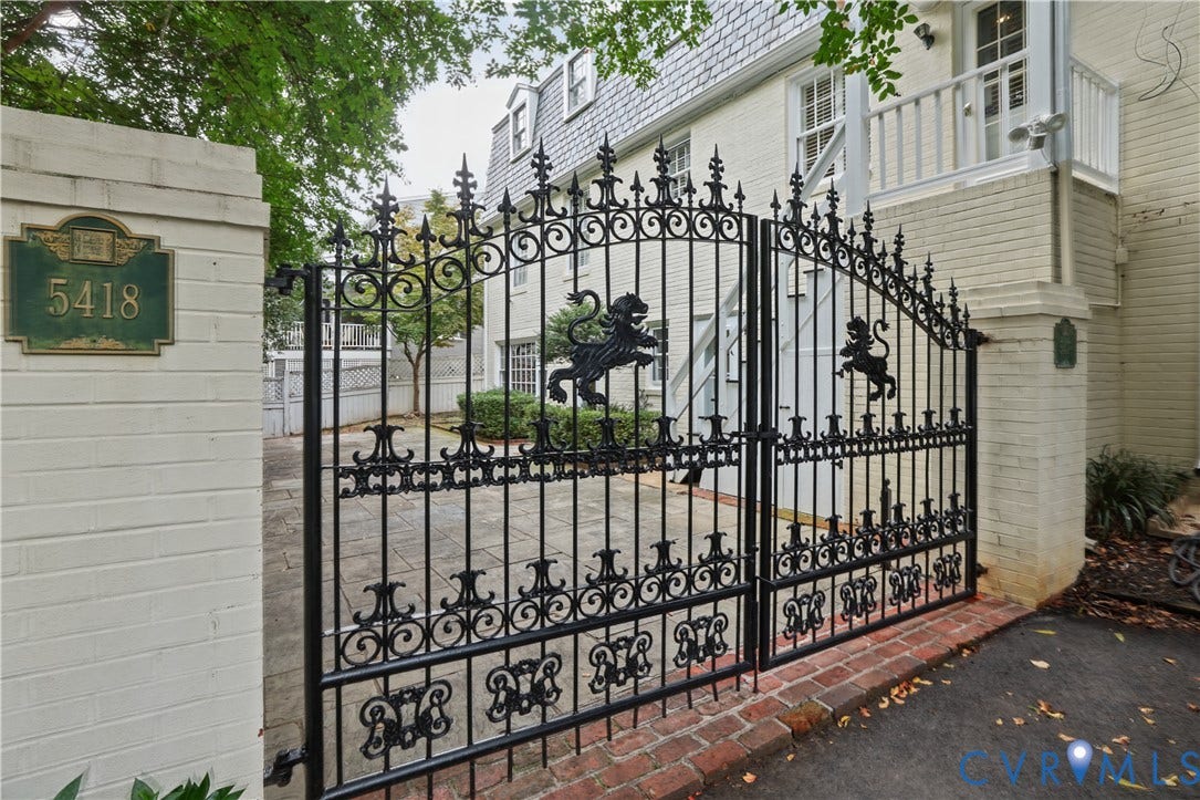 5418 Cary Street Road, Richmond, VA 23226 Ornate black wrought iron entry gates featuring lion crest motifs, set between brick pillars, leading to a stone-paved courtyard and a brick exterior with a mansard roof