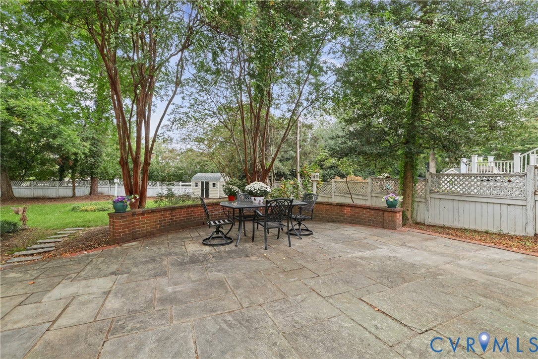 5418 Cary Street Road, Richmond, VA 23226 Flagstone patio featuring a low-profile brick retaining wall, mature trees, lattice-style fencing, and a detached storage structure