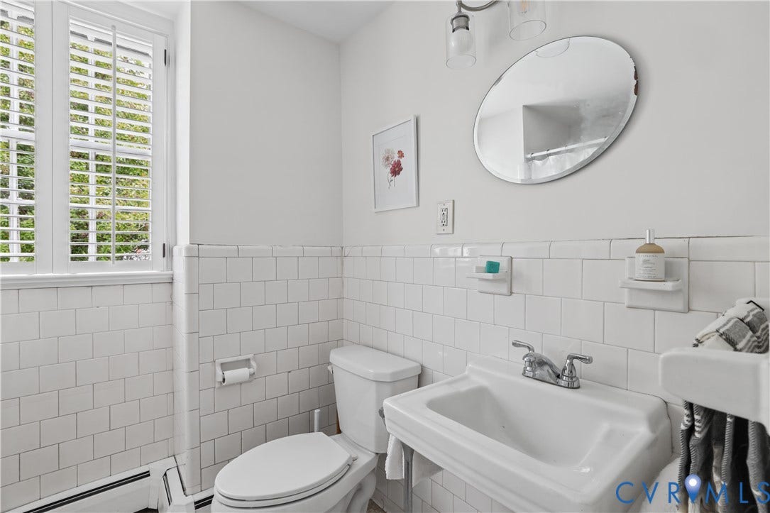 5418 Cary Street Road, Richmond, VA 23226 Wall-mounted porcelain sink with dual-handle metal faucet, oval wall mirror, white subway tile wainscoting, and window with built-in shutters