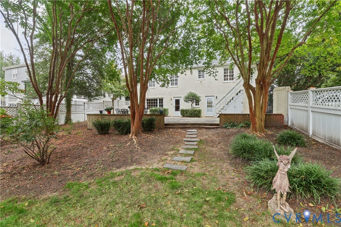 5418 Cary Street Road, Richmond, VA 23226 Backyard featuring a paved stone patio, retaining wall, stone paver pathway, mature trees, and white lattice fencing
