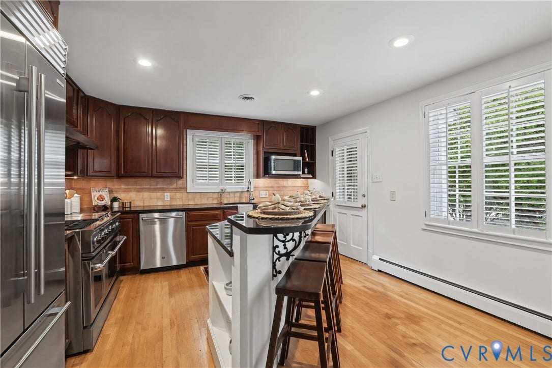 5418 Cary Street Road, Richmond, VA 23226 Kitchen featuring dark wood cabinetry, black countertops, stainless steel appliances, wood-finish flooring, and plantation shutters
