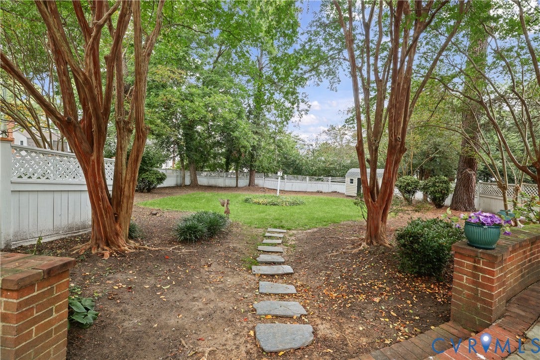 5418 Cary Street Road, Richmond, VA 23226 Spacious backyard featuring mature trees, a central lawn area, stone pathway, brick retaining wall, and white lattice fencing
