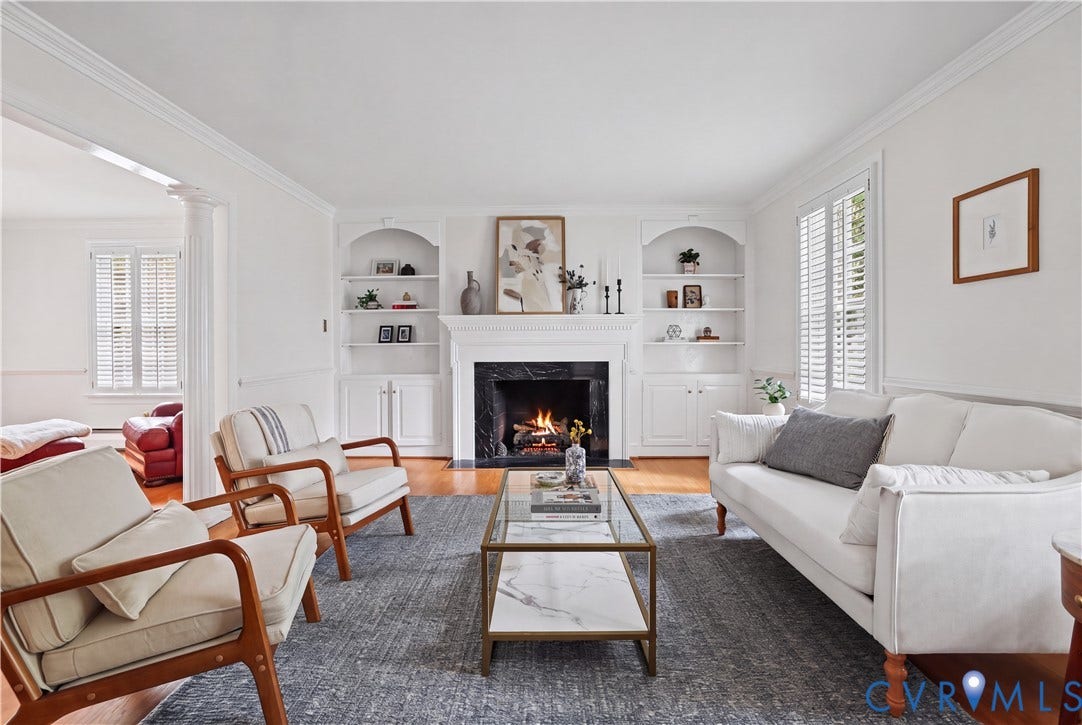 5418 Cary Street Road, Richmond, VA 23226 Living room featuring polished wood-finish flooring, built-in recessed cabinetry, crown molding, plantation shutters, and a fireplace with a stone surround