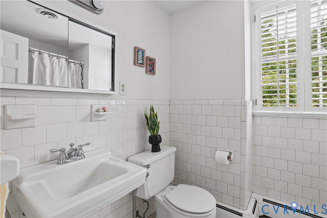 5418 Cary Street Road, Richmond, VA 23226 Wall-mounted medicine cabinet with a mirror, porcelain wall-mounted sink with chrome dual-handle faucet, white subway tile wainscoting, and shuttered windows