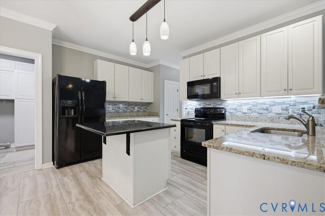 Contemporary kitchen featuring a central island with a dark countertop, light-toned cabinetry, light wood-finish flooring, black appliances, and a tiled backsplash