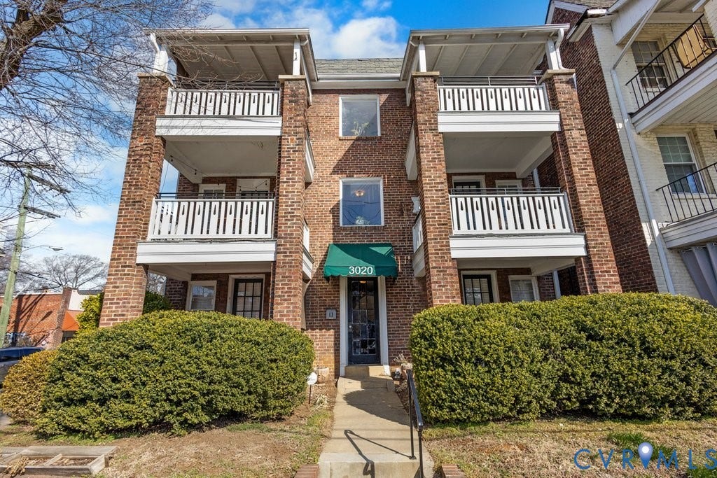 3020 Patterson Avenue, #U8, Museum District, Richmond, VA 23221 Brick facade apartment building featuring multiple balconies with white railings, a front entrance with an awning, and established shrubbery