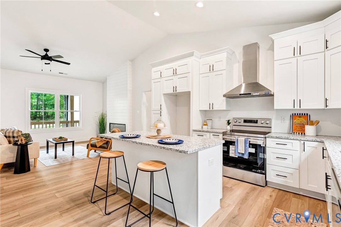 716 Pine Harbour Drive, Pine Harbour, Mineral, VA 23117 Open-concept living space featuring a white kitchen island, light wood-finish flooring, white cabinetry with dark hardware, stainless steel appliances, and a built-in fireplace