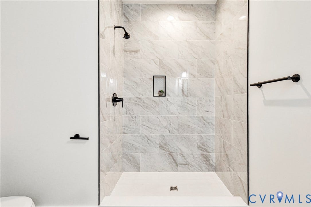 716 Pine Harbour Drive, Pine Harbour, Mineral, VA 23117 Walk-in shower featuring large format tile with naturalistic veining, matte black fixtures, a built-in shower niche, and a white shower pan