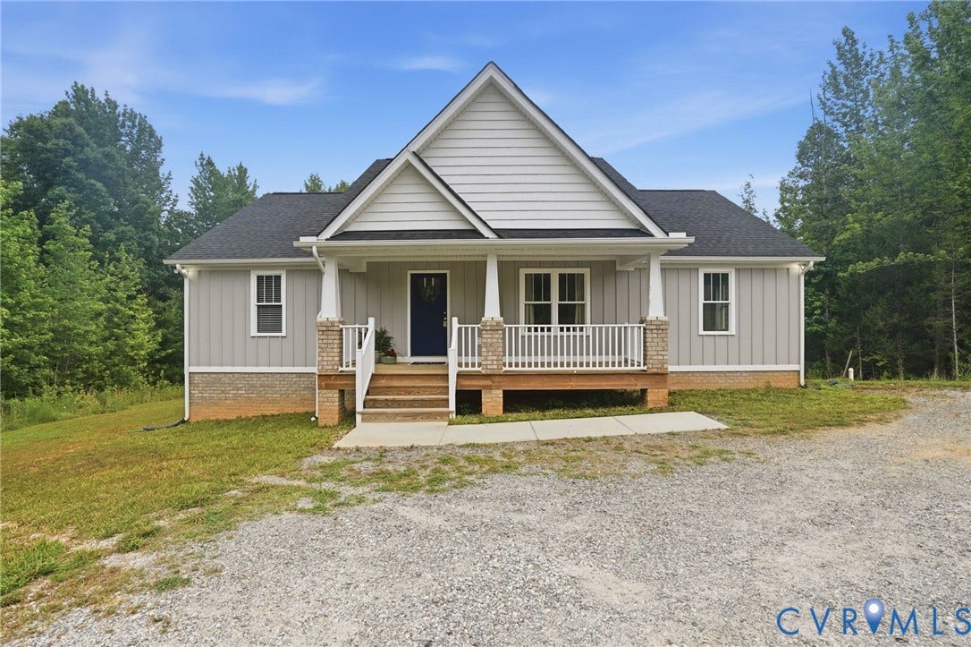 2677 Dogtown Road, Goochland, VA 23063 Craftsman-style home featuring light gray vertical siding, a dark blue entry door, and a covered front porch with white railings and brick-accented columns