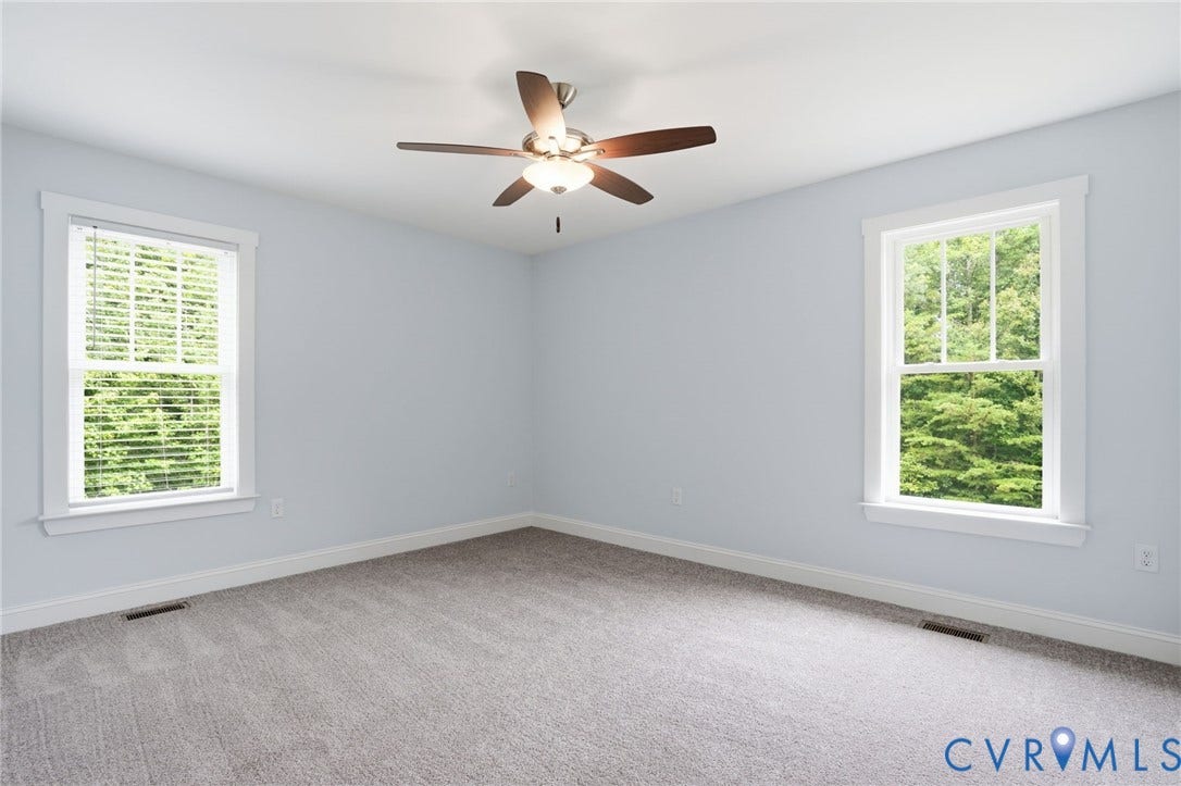 2677 Dogtown Road, Goochland, VA 23063 Spacious room featuring light blue walls, gray carpet, two windows with white trim, and a ceiling fan with integrated lighting