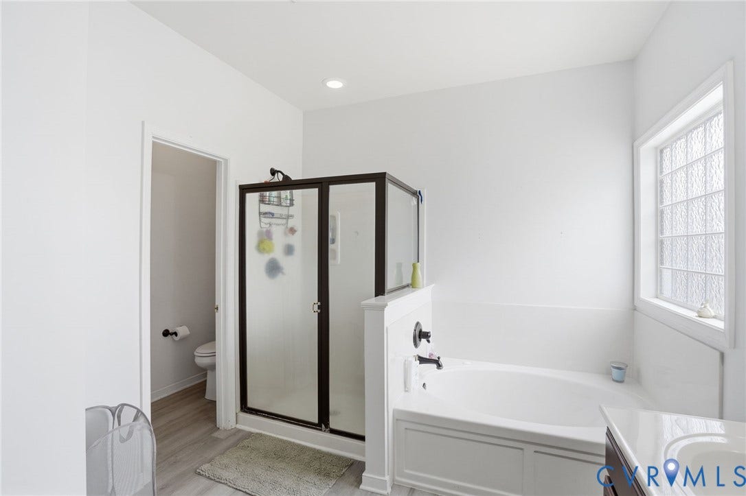 5305 Wellington Ridge Road, Richmond, VA 23231 Bathroom featuring a dark-framed shower enclosure, a white soaking tub, and a window with textured glass