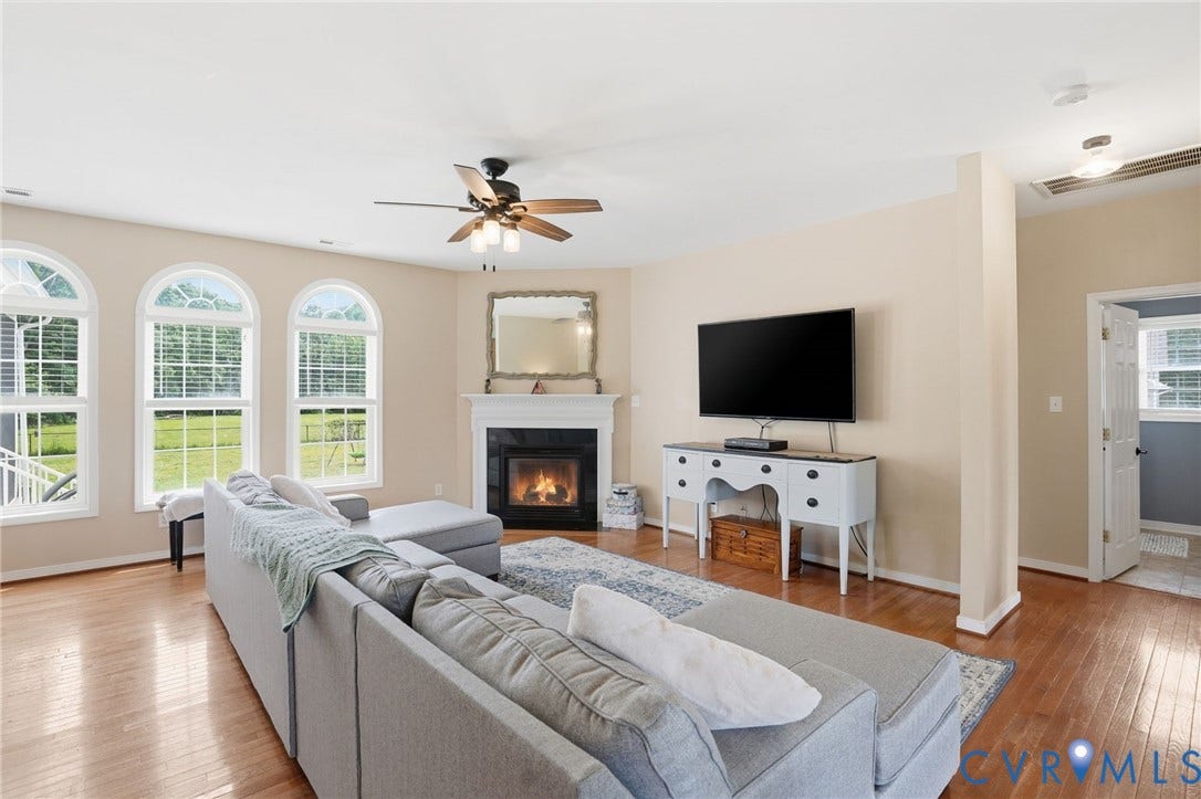 5305 Wellington Ridge Road, Richmond, VA 23231 Living area featuring hardwood flooring, a fireplace with a white mantel, and three arched windows with outdoor views