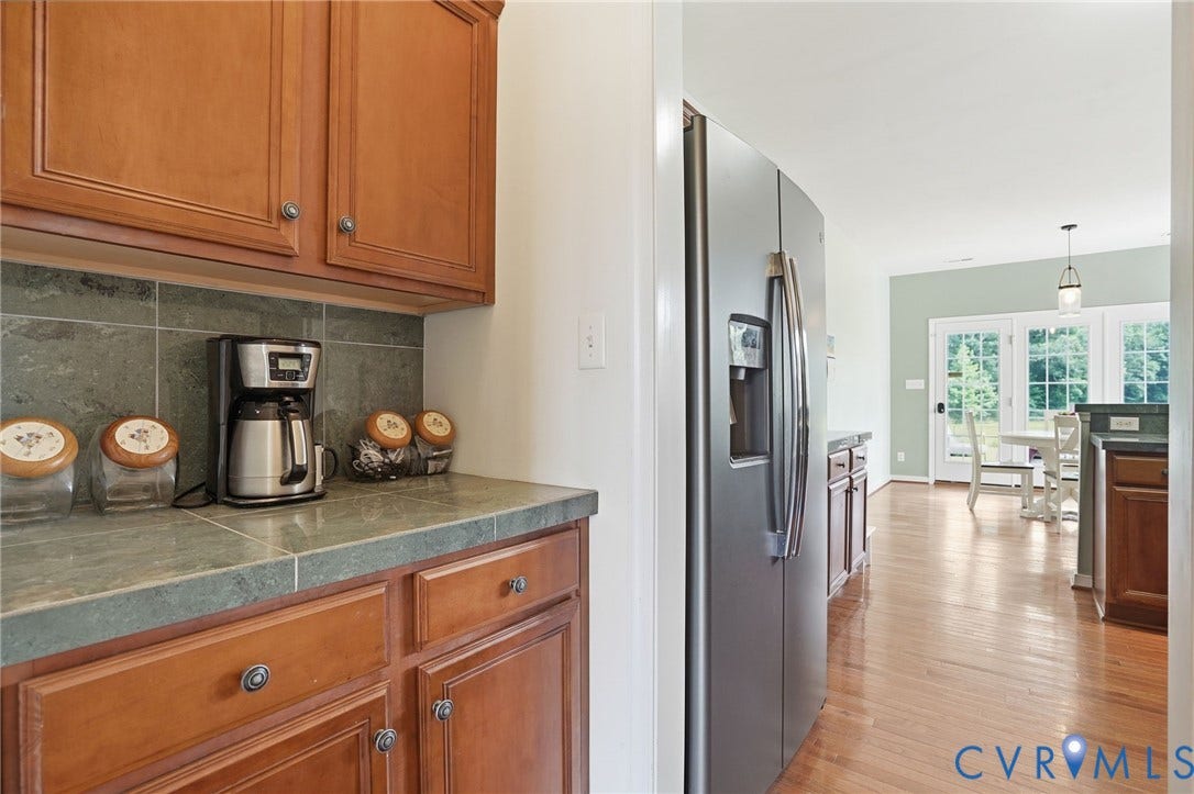 5305 Wellington Ridge Road, Richmond, VA 23231 Kitchen area featuring warm wood cabinetry, a dark tiled backsplash, and stone-finish countertops