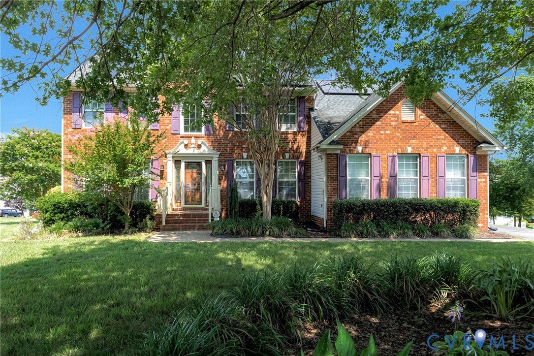 Brick facade residence featuring a covered entry porch with white railings, purple window shutters, a gabled roofline, and established landscaping