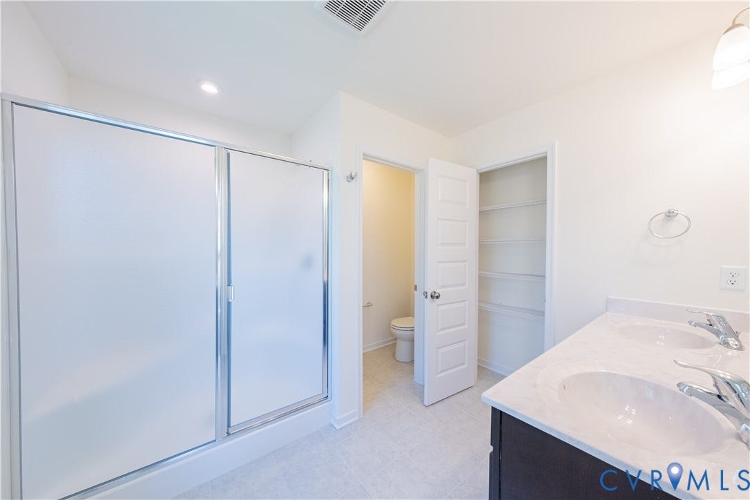 18372 Palisades Court, Chesterfield, VA 23120 Bathroom featuring a frosted glass shower enclosure with chrome hardware, a dual-sink vanity with a light-colored countertop, dark wood-finish cabinetry, and light-toned tile flooring