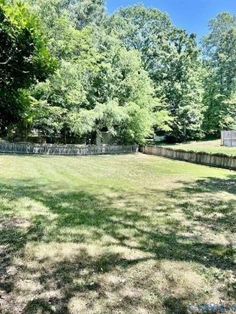 Expansive grassy yard area featuring mature tree perimeter and wood fencing