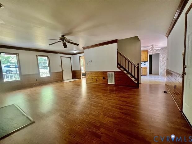 Spacious living area featuring wood-finish flooring, wainscoting, and a ceiling fan
