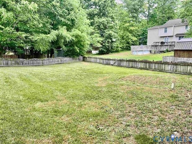 Expansive backyard featuring a wood fence, mature trees, and a visible portion of an above-ground pool with surrounding deck