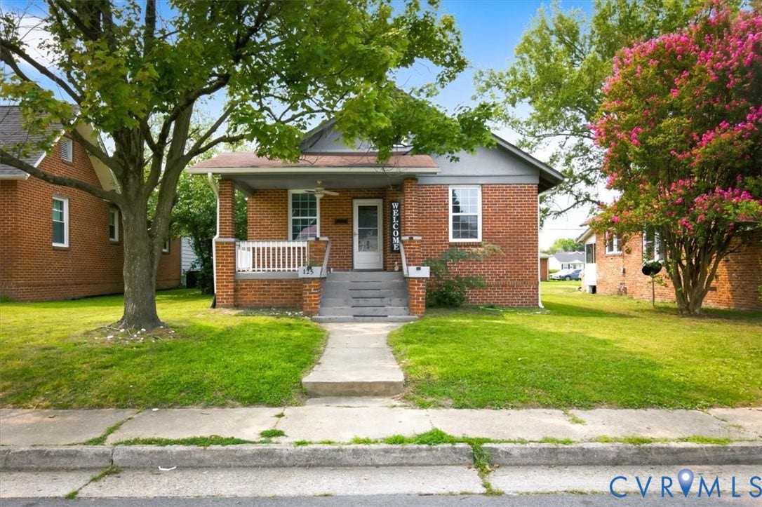 125 Richmond Avenue, Colonial Heights, VA 23834 Brick exterior featuring a covered front porch with white railing, a concrete walkway, and mature trees